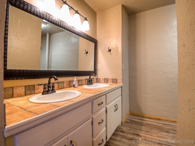 bathroom with double vanity, wood finished floors, a sink, and a textured wall