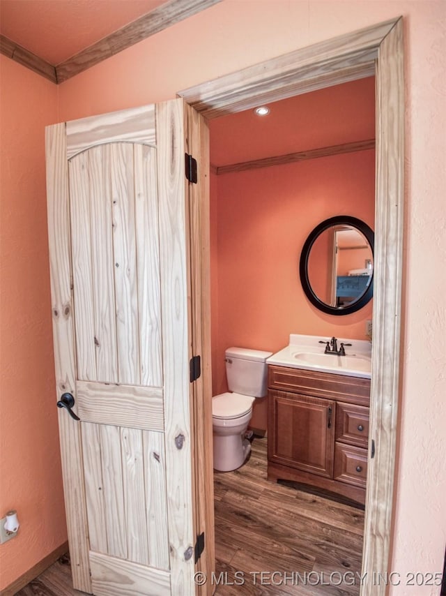 half bathroom featuring vanity, wood finished floors, toilet, and crown molding