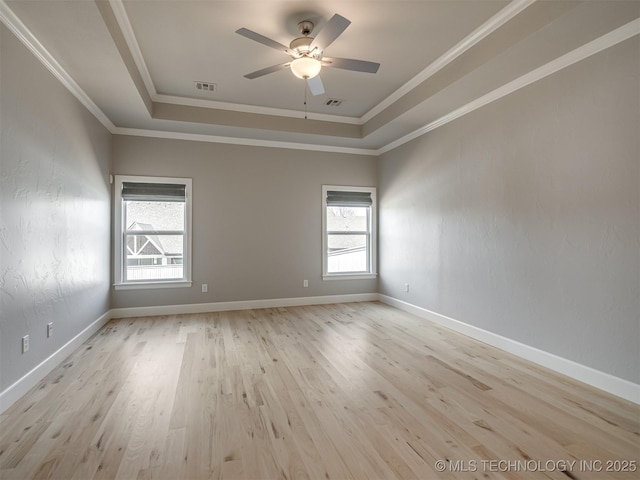 spare room with a tray ceiling, visible vents, ornamental molding, light wood-type flooring, and baseboards