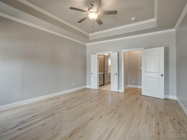 unfurnished bedroom featuring baseboards, ornamental molding, light wood-type flooring, a raised ceiling, and ensuite bath