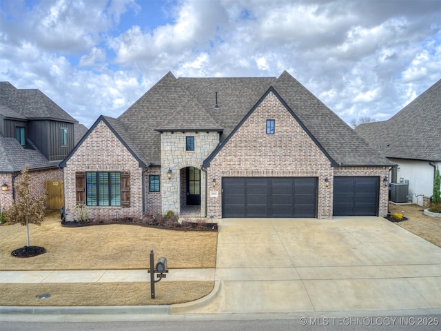 french country inspired facade with stone siding, roof with shingles, concrete driveway, and brick siding