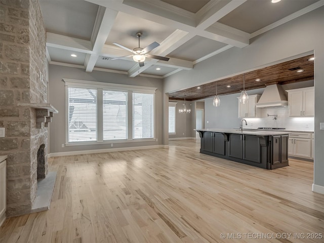 kitchen with light wood-style flooring, open floor plan, beamed ceiling, custom exhaust hood, and a sink