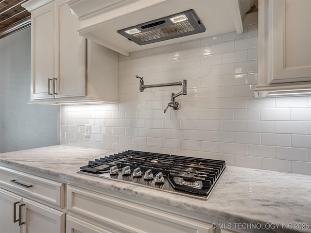 kitchen with light stone countertops, tasteful backsplash, stainless steel gas stovetop, and exhaust hood