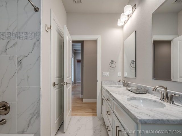 bathroom with marble finish floor, double vanity, walk in shower, and a sink