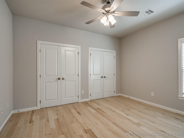 unfurnished bedroom featuring light wood finished floors, baseboards, visible vents, and two closets