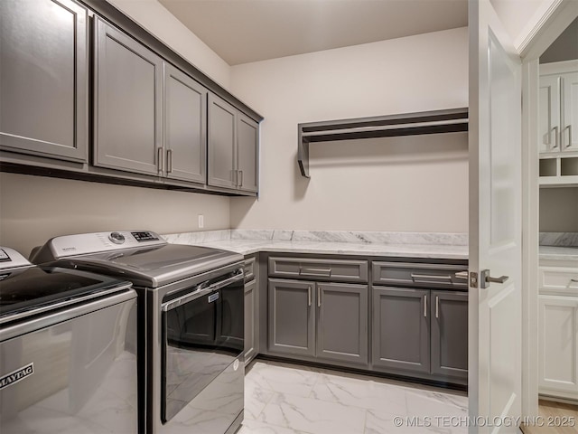 clothes washing area with washing machine and dryer, marble finish floor, and cabinet space