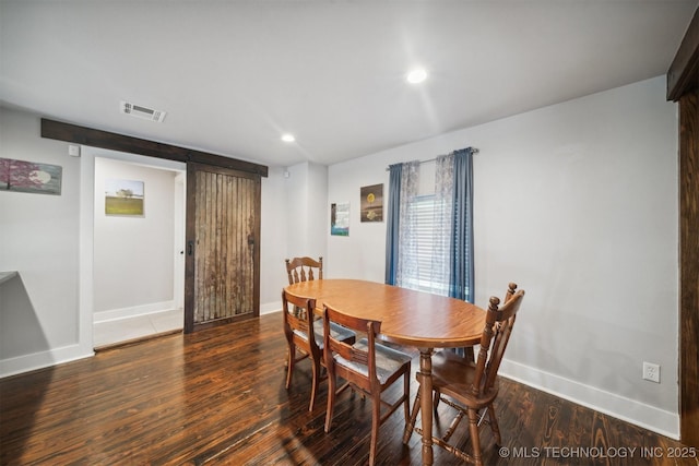 dining space featuring a barn door, wood finished floors, visible vents, and baseboards