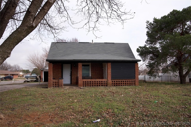 view of front facade featuring brick siding, fence, covered porch, and a front yard