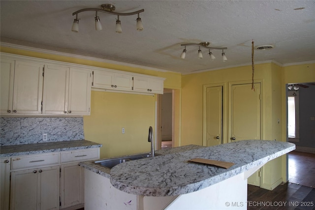 kitchen featuring a kitchen island with sink, dark wood-type flooring, a sink, white cabinetry, and ornamental molding