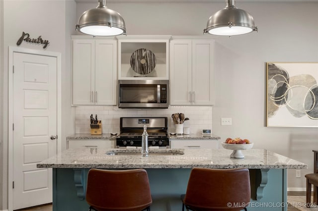 kitchen featuring range with gas cooktop, stainless steel microwave, backsplash, and white cabinets