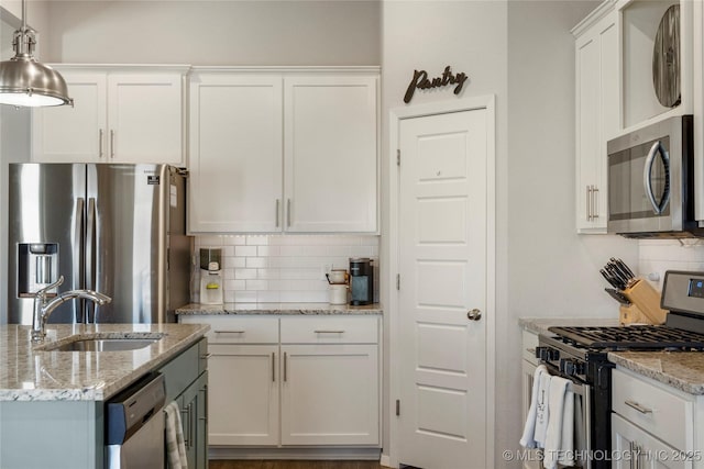 kitchen featuring tasteful backsplash, white cabinets, stainless steel appliances, pendant lighting, and a sink