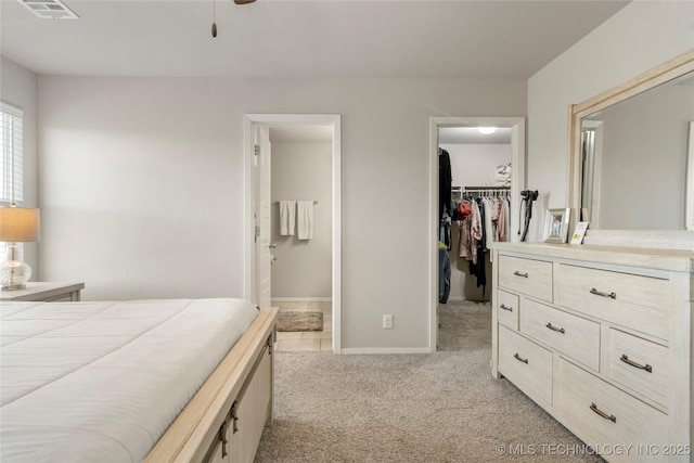 bedroom featuring a walk in closet, a closet, light colored carpet, visible vents, and ensuite bath