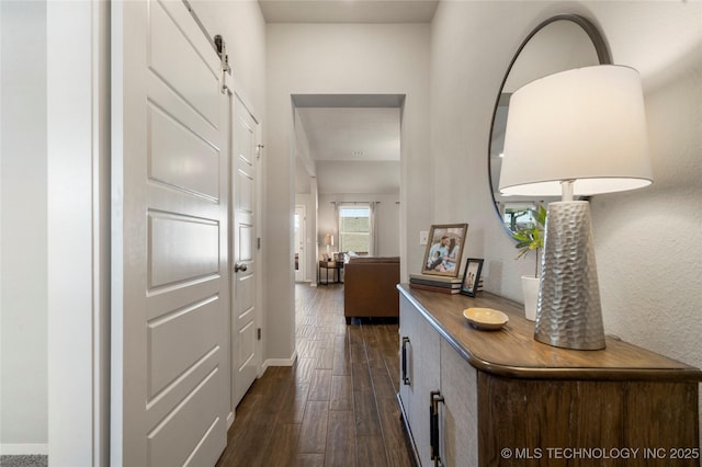 hallway with a barn door, baseboards, and dark wood-type flooring