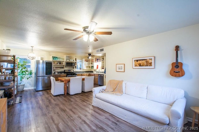 living room with a ceiling fan, visible vents, dark wood finished floors, and a textured ceiling