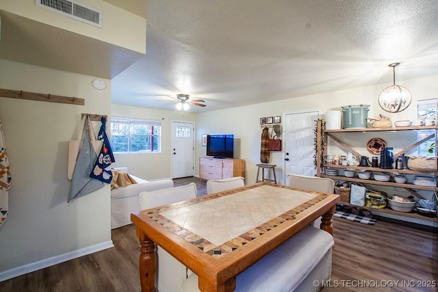 dining area featuring a textured ceiling, ceiling fan with notable chandelier, wood finished floors, visible vents, and baseboards