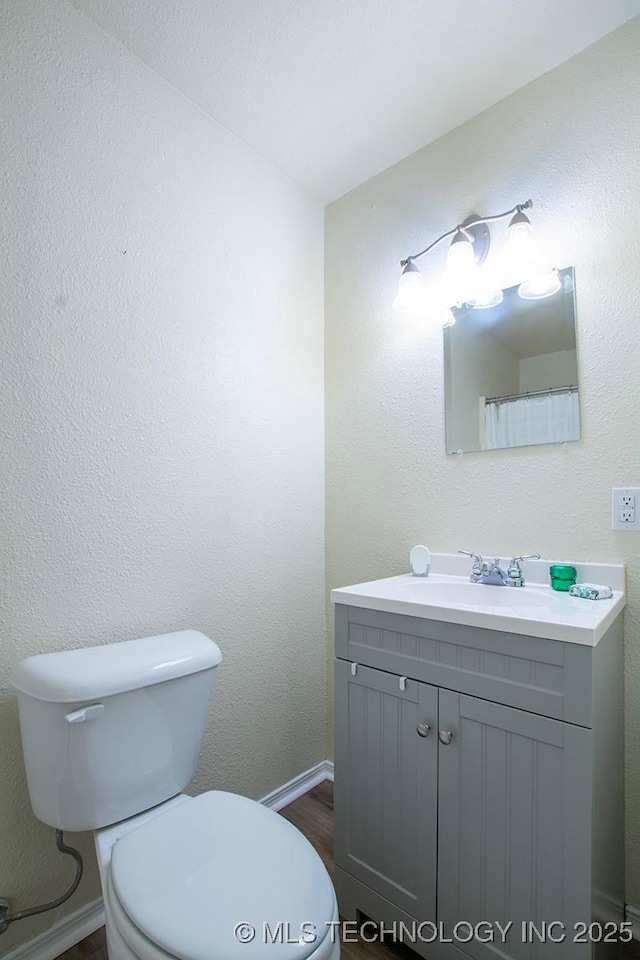 bathroom with baseboards, a textured wall, vanity, and toilet