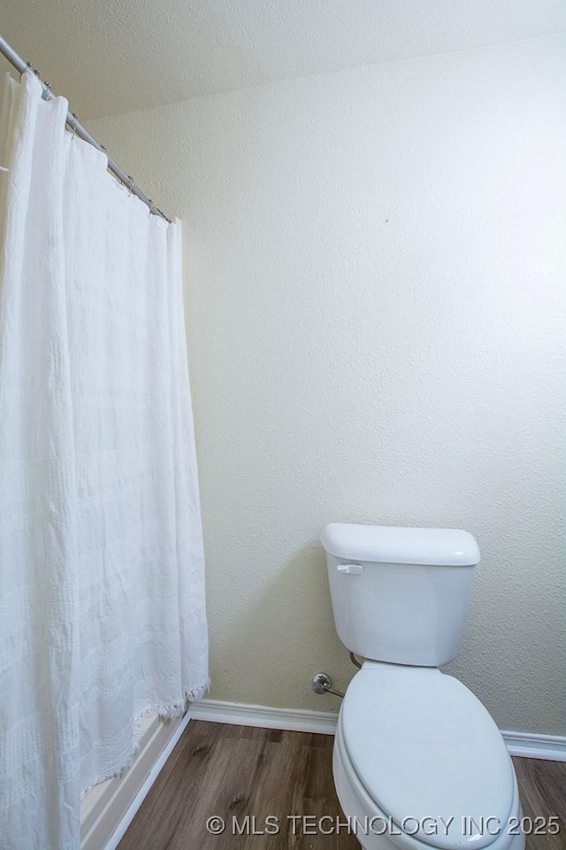 bathroom with a textured wall, toilet, baseboards, and wood finished floors