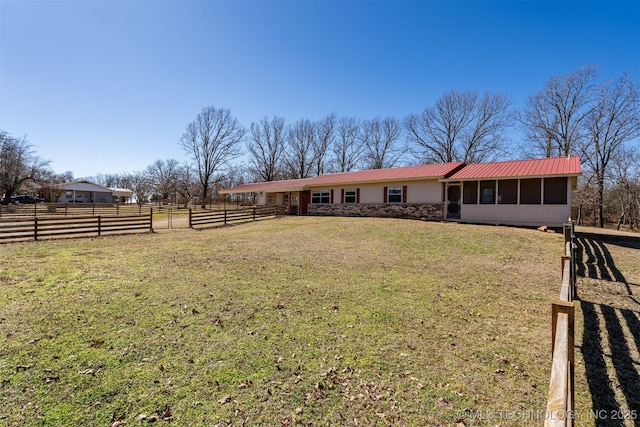 view of front facade with metal roof, fence, a sunroom, stone siding, and a front yard