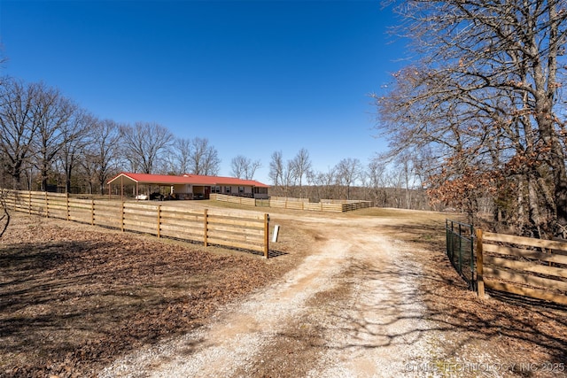 view of street with dirt driveway, a gated entry, an outbuilding, and a rural view