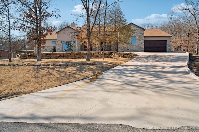 view of front of home featuring a garage, driveway, stone siding, a chimney, and stucco siding