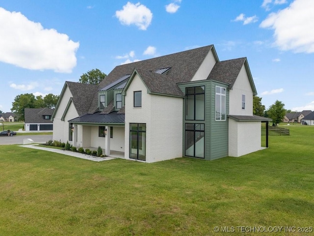 back of property with metal roof, a shingled roof, a standing seam roof, and a lawn