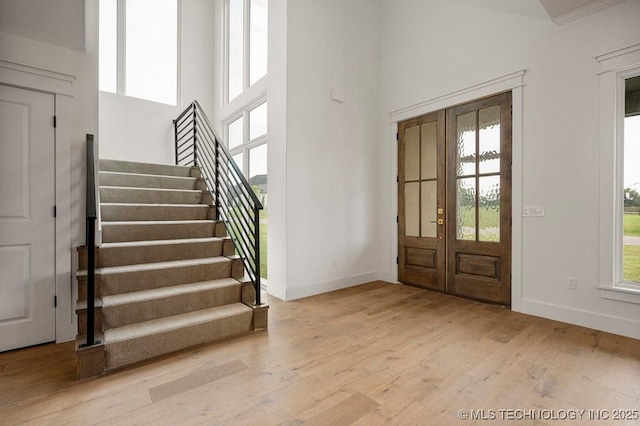 entrance foyer with stairway, a towering ceiling, light wood-style flooring, and baseboards