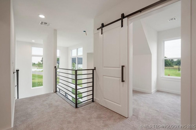 corridor with an upstairs landing, visible vents, and light colored carpet