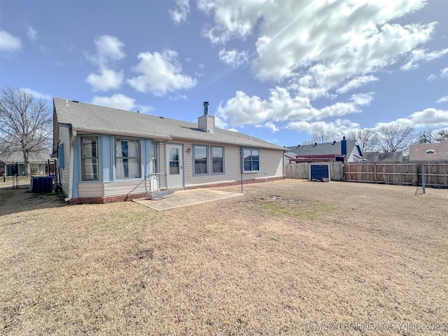 back of house featuring a lawn, fence, a chimney, and central air condition unit