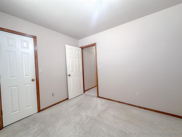 unfurnished bedroom featuring light carpet, a textured ceiling, and baseboards