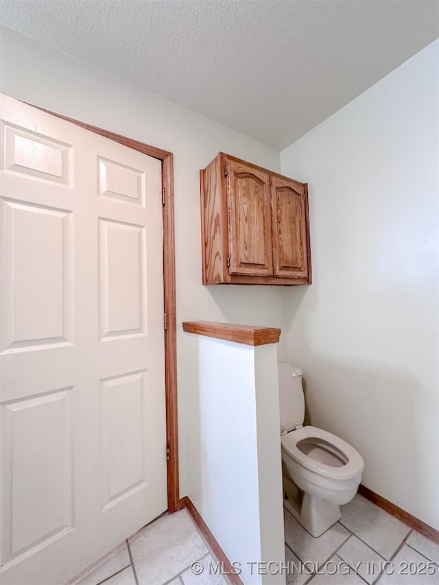 bathroom featuring a textured ceiling, tile patterned floors, toilet, and baseboards