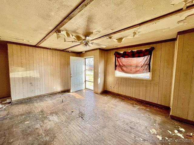 empty room featuring ceiling fan, wooden walls, baseboards, and a textured ceiling