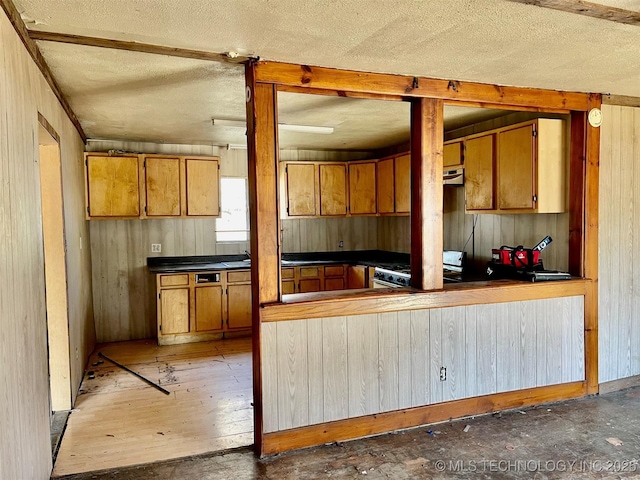 kitchen featuring brown cabinetry, wood walls, a textured ceiling, and white gas range