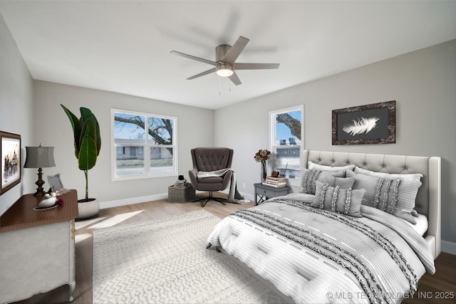 bedroom with ceiling fan, multiple windows, baseboards, and wood finished floors