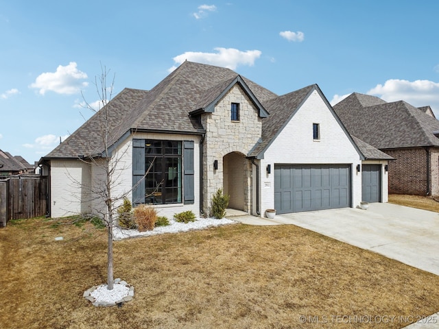 french country style house featuring brick siding, a shingled roof, concrete driveway, fence, and a front lawn