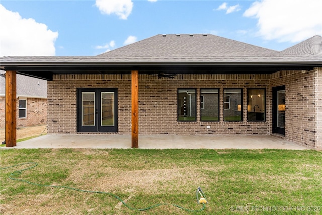 rear view of property with brick siding, a patio area, a lawn, and a shingled roof