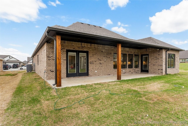 back of house with brick siding, a yard, a patio area, and roof with shingles