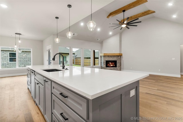 kitchen featuring a sink, light wood-type flooring, a ceiling fan, gray cabinetry, and a fireplace