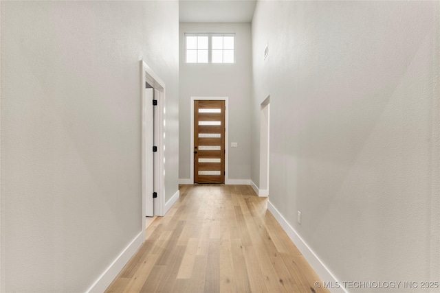 entryway with baseboards, a towering ceiling, and light wood-type flooring