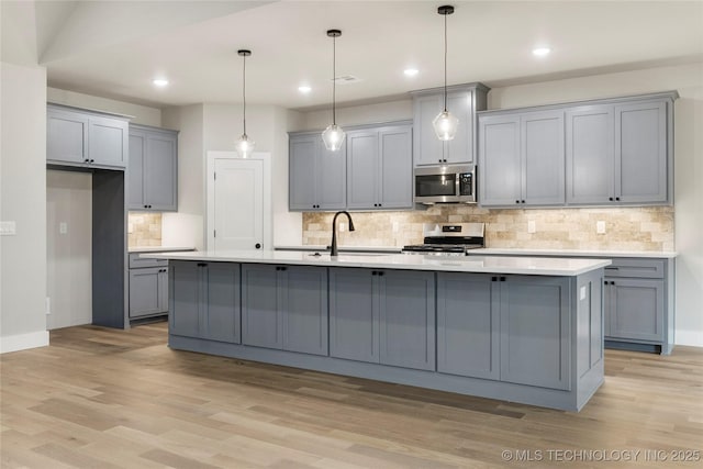 kitchen with gray cabinets, stainless steel appliances, light wood-type flooring, and a sink