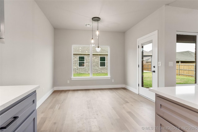 unfurnished dining area with light wood finished floors, plenty of natural light, baseboards, and visible vents