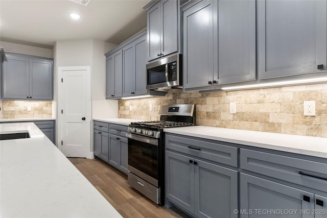 kitchen featuring light countertops, dark wood finished floors, backsplash, appliances with stainless steel finishes, and gray cabinetry