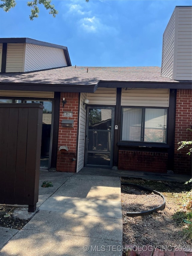 view of exterior entry with roof with shingles and brick siding