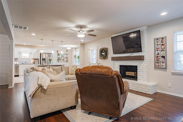 living room featuring a wealth of natural light, dark wood-style flooring, a fireplace, and visible vents