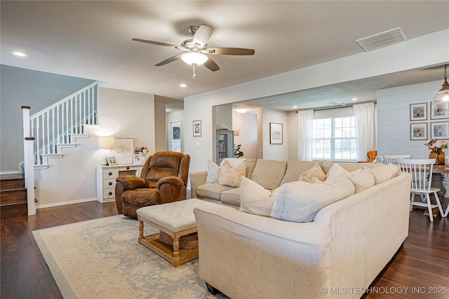 living area with stairway, a ceiling fan, visible vents, and dark wood-type flooring