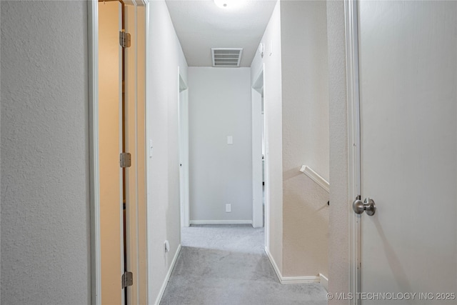 corridor featuring a textured wall, carpet flooring, visible vents, and baseboards