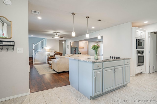 kitchen with a center island, decorative light fixtures, visible vents, appliances with stainless steel finishes, and light stone countertops