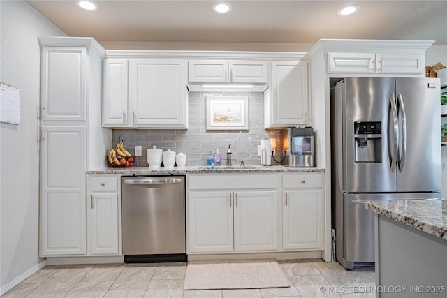 kitchen with backsplash, white cabinetry, stainless steel appliances, and light stone counters