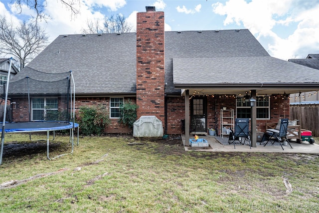 back of house with a lawn, a patio, a chimney, roof with shingles, and a trampoline