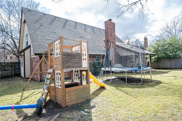 rear view of house featuring a playground, a shingled roof, fence, a lawn, and a trampoline