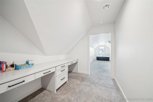 office area featuring light carpet, visible vents, baseboards, vaulted ceiling, and built in study area